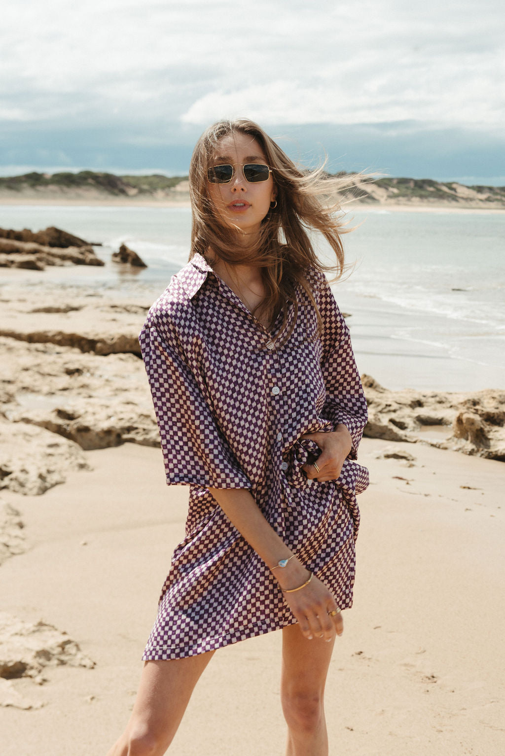 Woman in a checkered dress standing on a beach with ocean and sky in the background