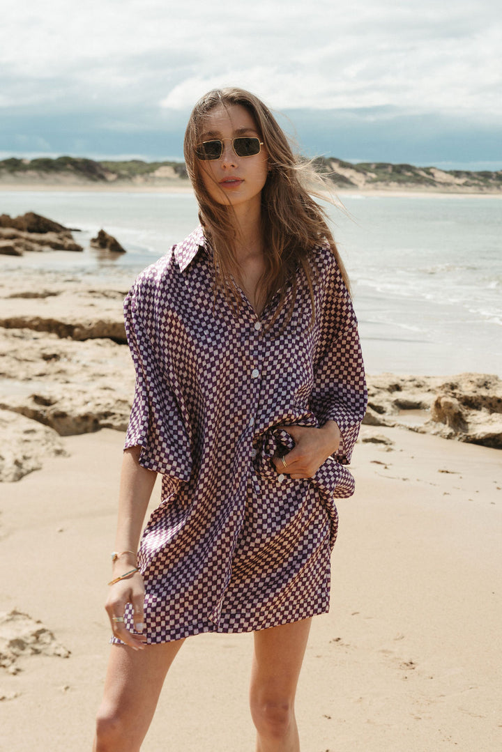Woman in a checkered dress standing on a beach with ocean and sky in the background