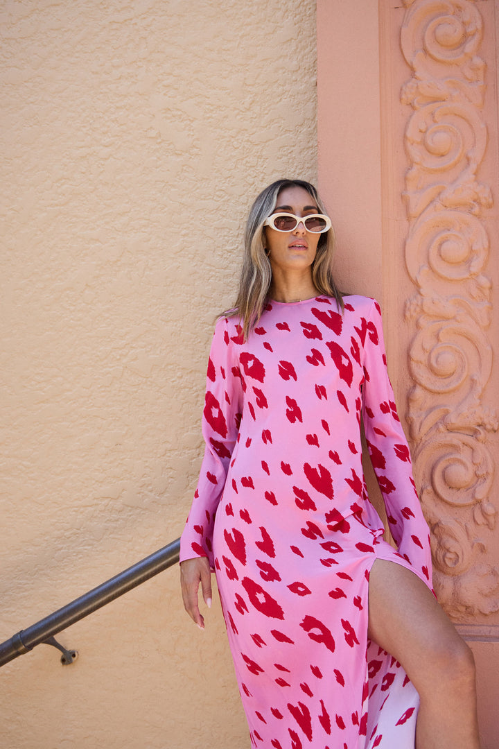 Woman wearing a pink dress with red patterns against a beige wall.