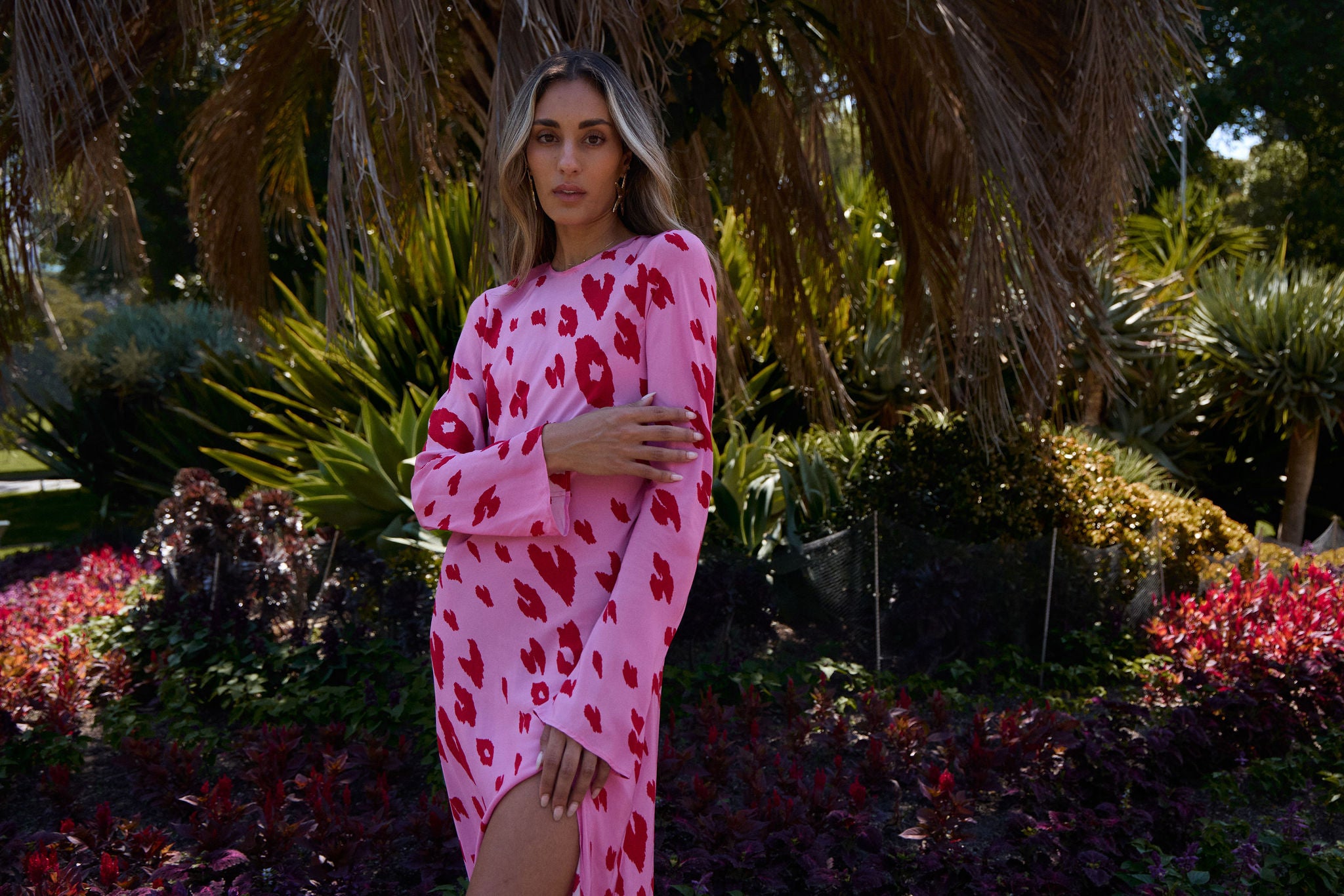 Woman in a pink dress with red patterns standing in a garden.