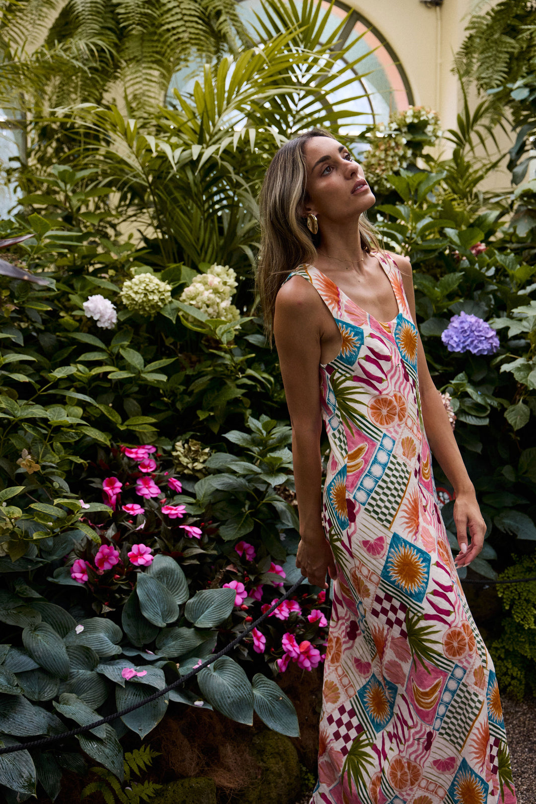 Woman in a colorful dress standing among lush greenery and flowers