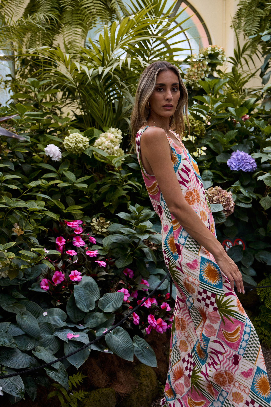 Woman in a colorful dress standing among lush greenery and flowers