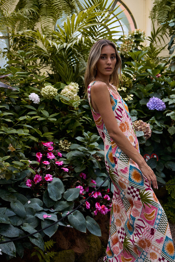 Woman in a colorful dress standing among lush greenery and flowers