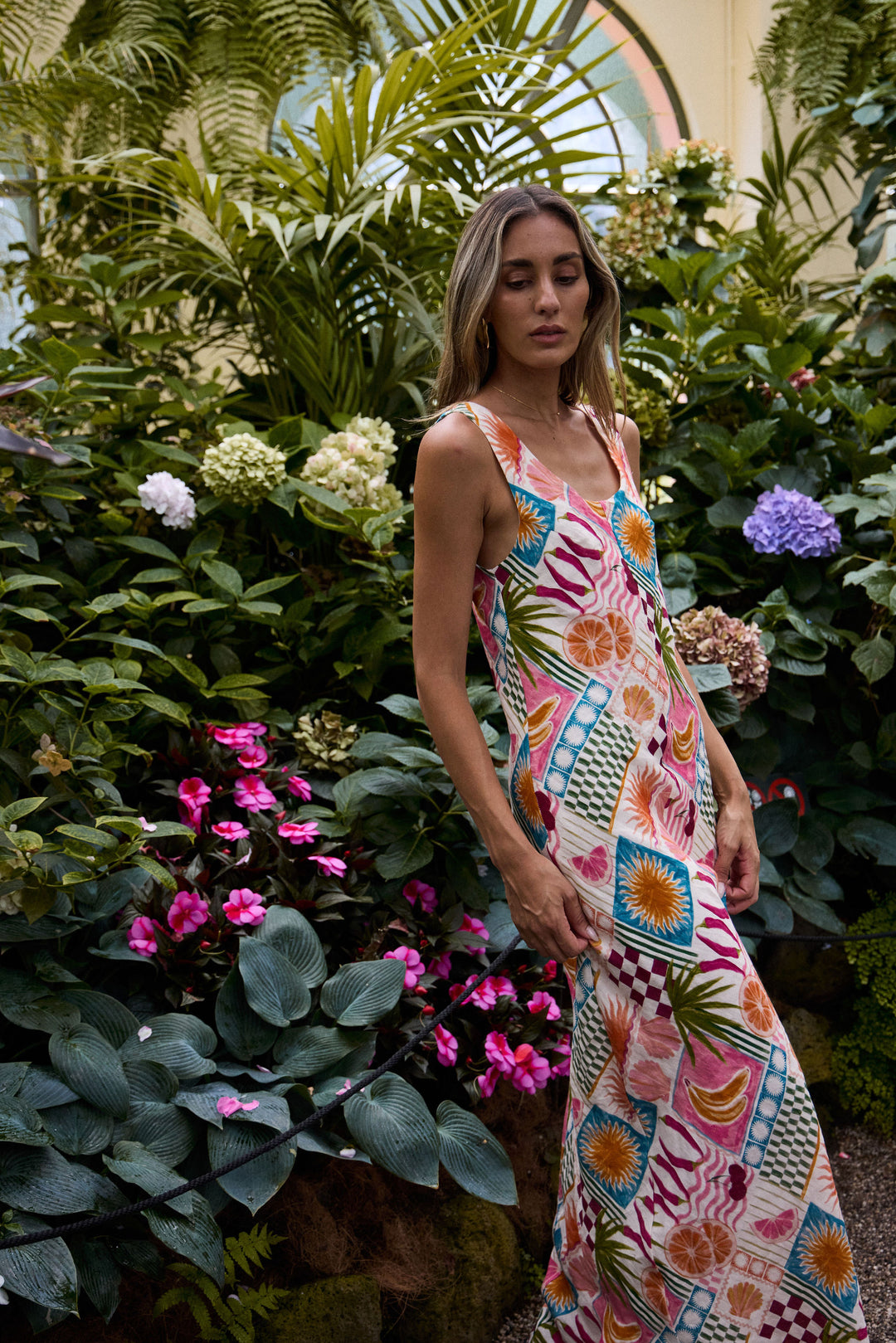 Woman in a colorful dress standing among lush greenery and flowers