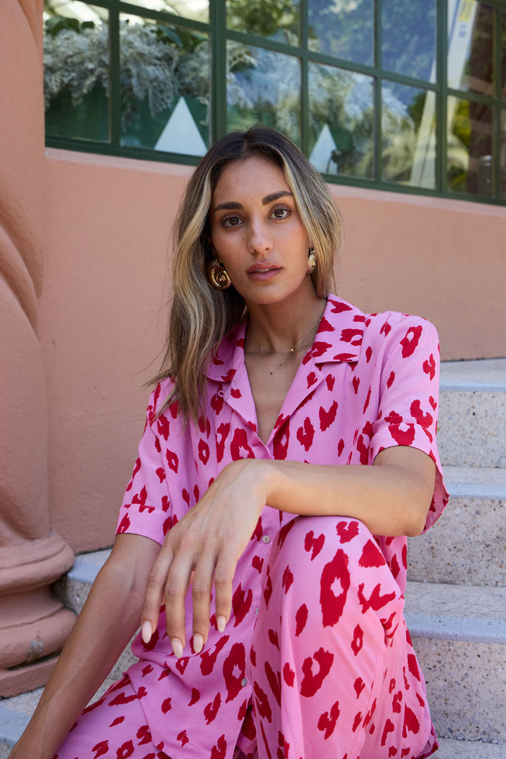 Woman in a pink dress with red patterns sitting on steps.
