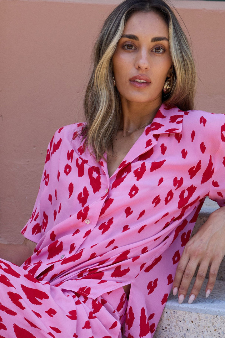 Woman in a pink outfit with red patterns sitting on steps outdoors.