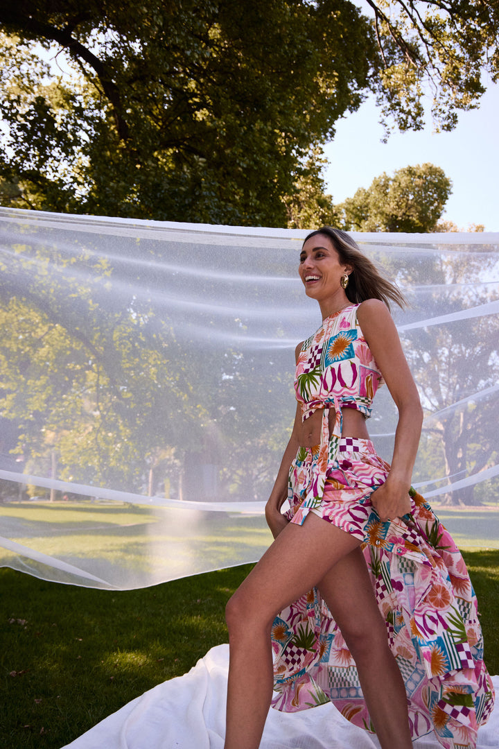 Woman in a colorful floral outfit standing outdoors with greenery in the background