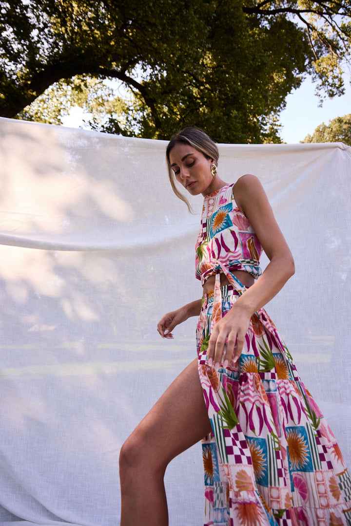 Woman in a colorful top and skirt standing outdoors with trees in the background