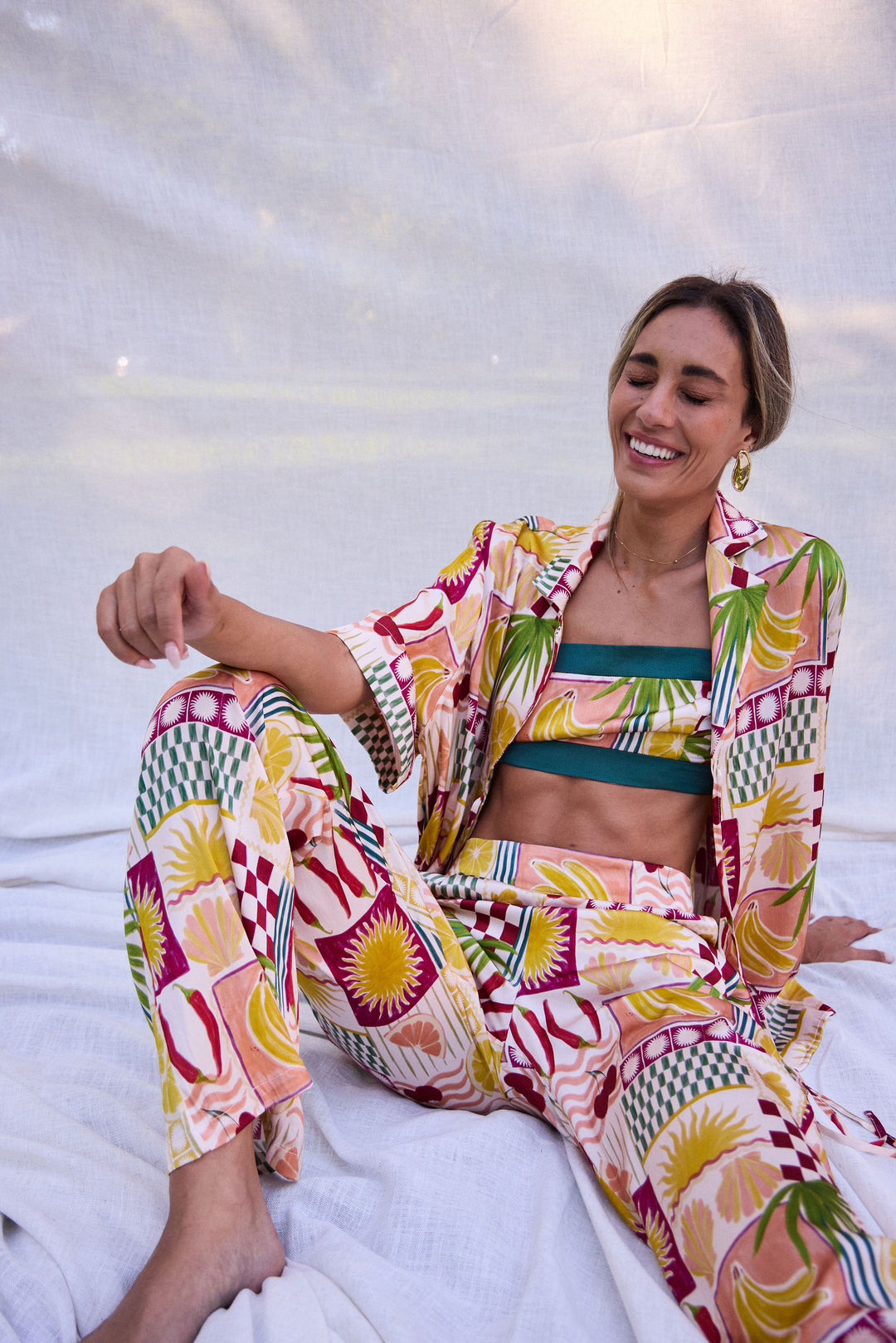 Woman wearing a colorful patterned outfit sitting on a white surface.