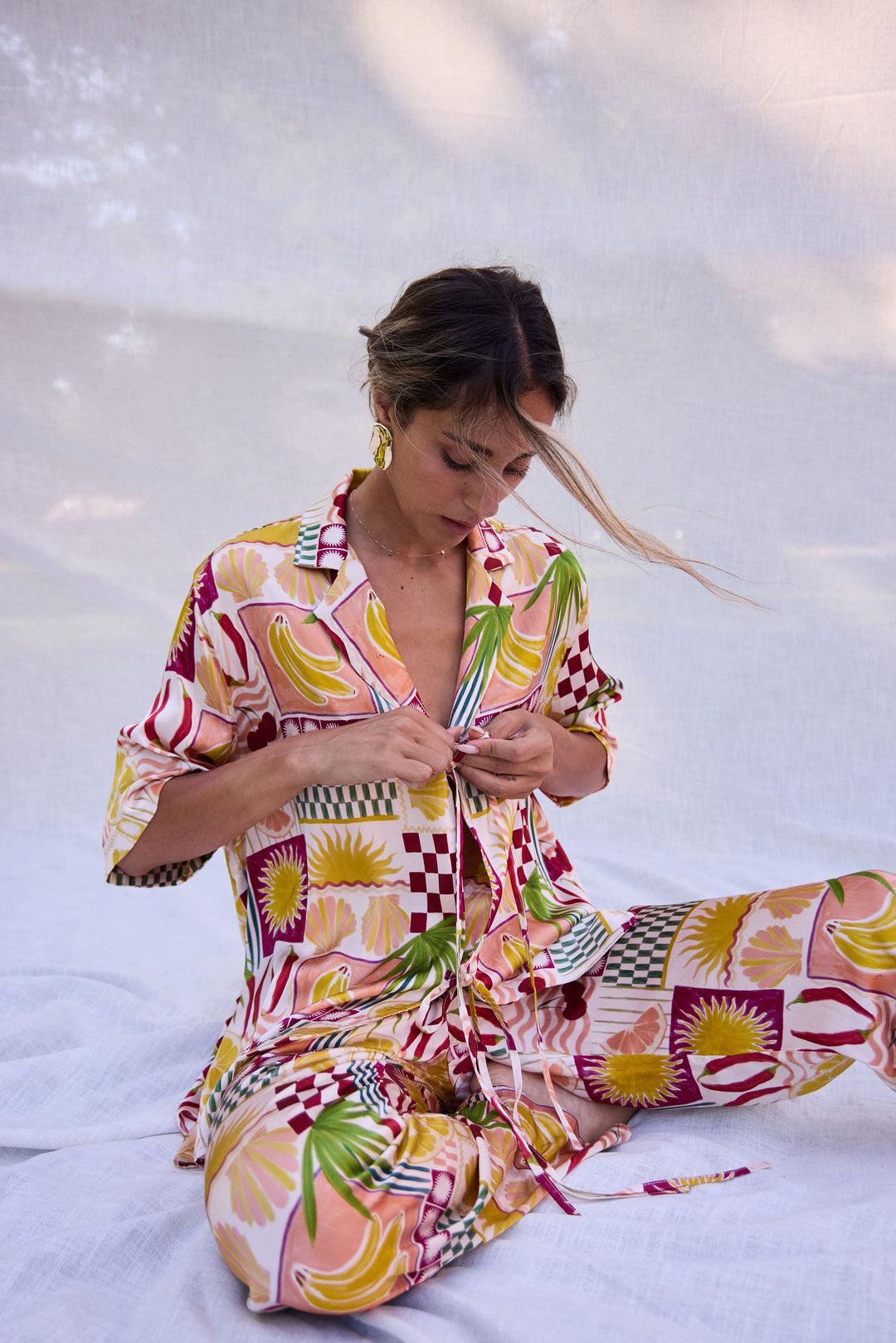 Woman wearing a colorful patterned outfit sitting on a white surface.