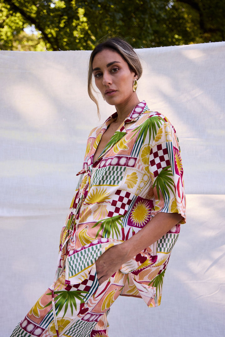 Woman wearing a colorful patterned dress standing against a white wall with greenery in the background