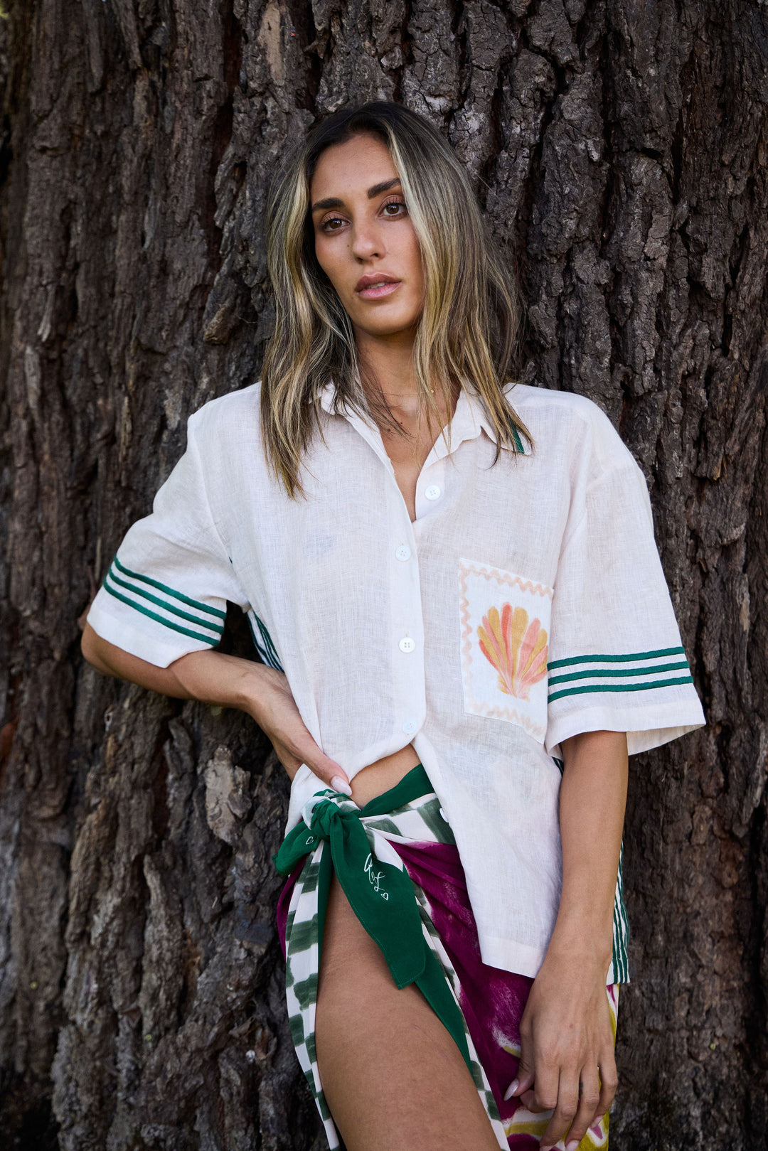 Woman in a white shirt with green accents standing against a tree