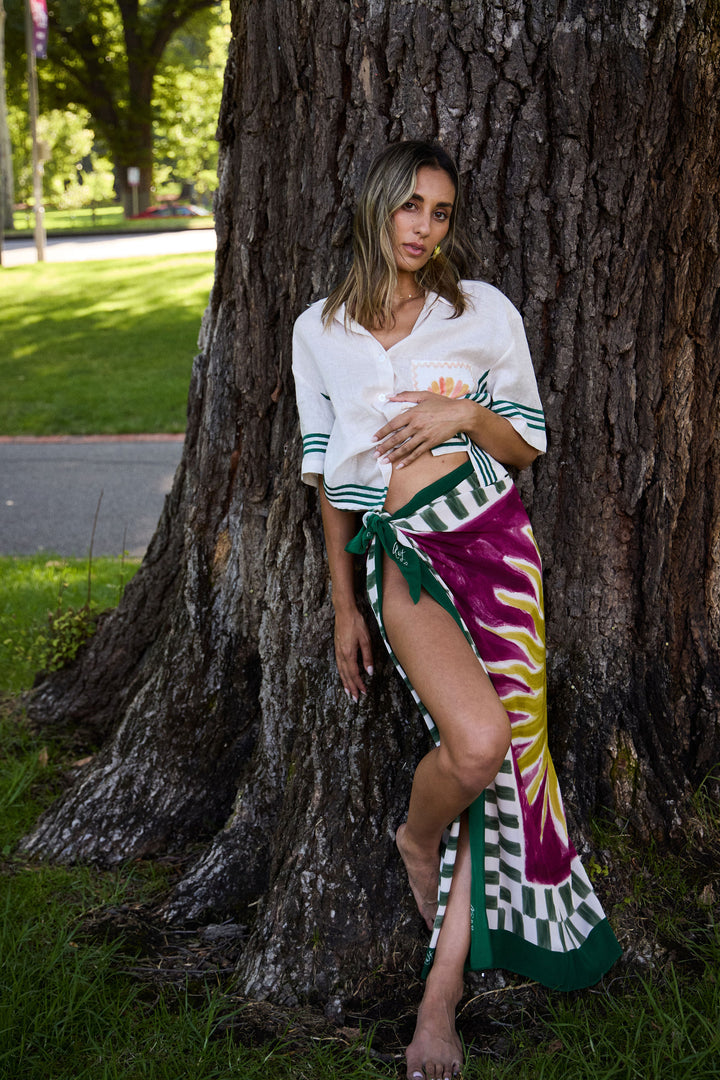 Woman standing next to a large tree wearing a colorful scarf and white top.