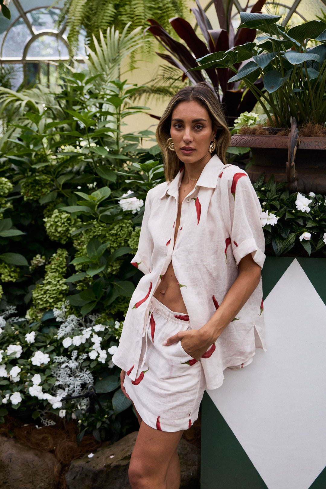 Woman in a white outfit with red accents standing in a lush garden.