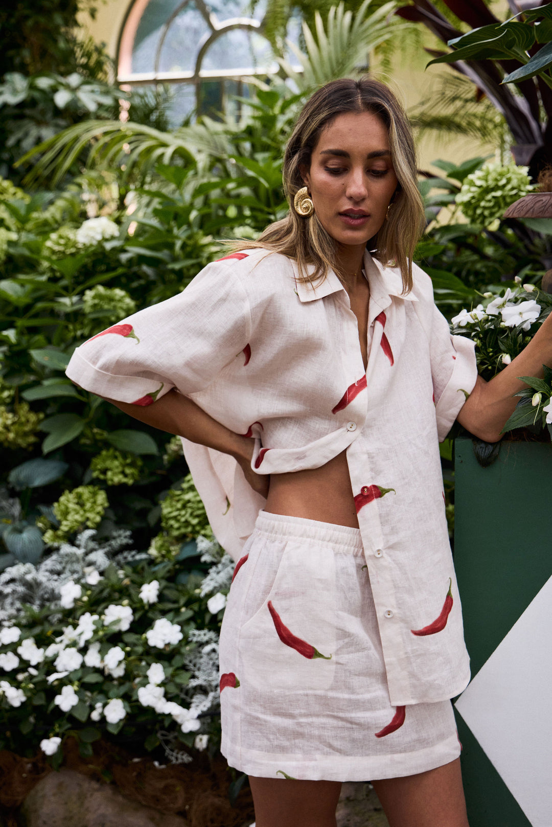 Woman wearing a white outfit with red chili pepper patterns in a garden setting