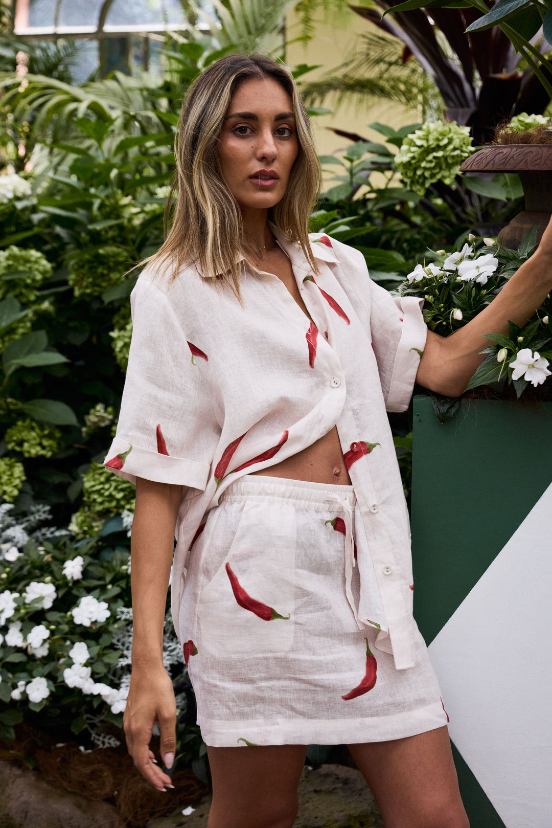 Woman wearing a white outfit with red chili pepper pattern in a garden setting