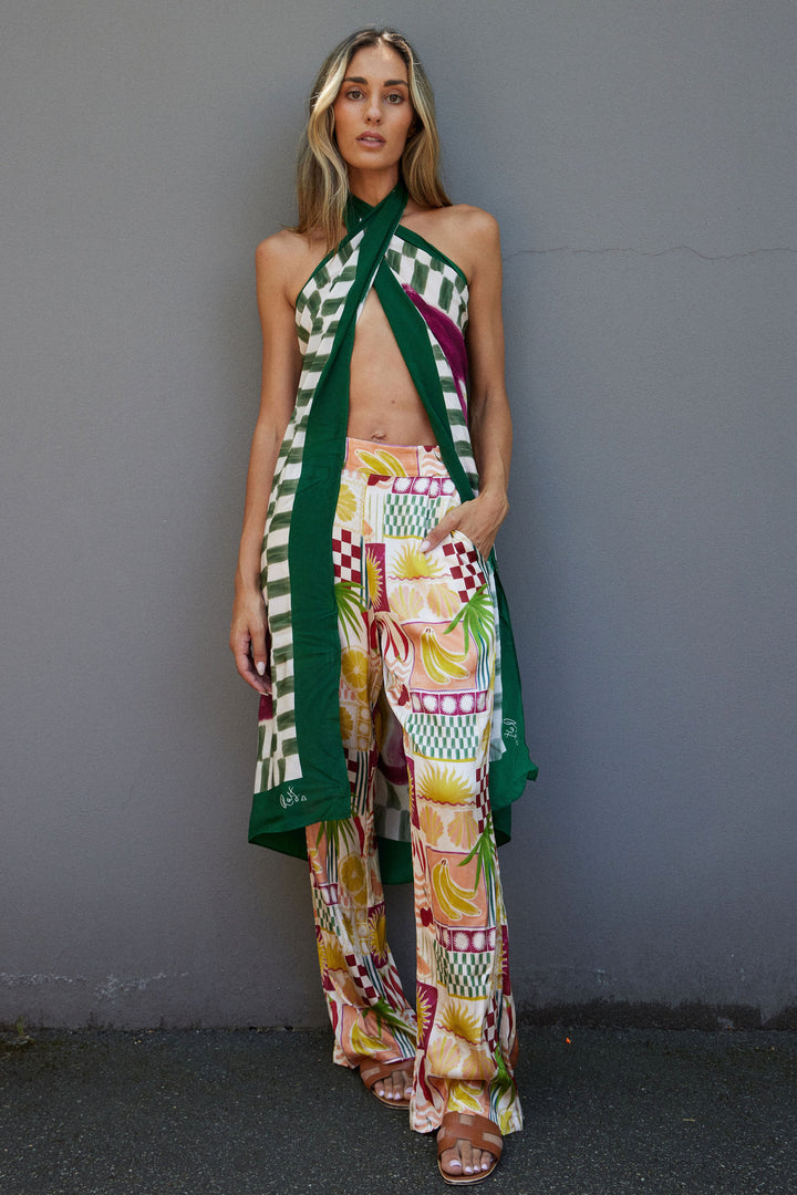 Woman wearing a colorful outfit with a patterned top and wide-leg pants against a gray wall.