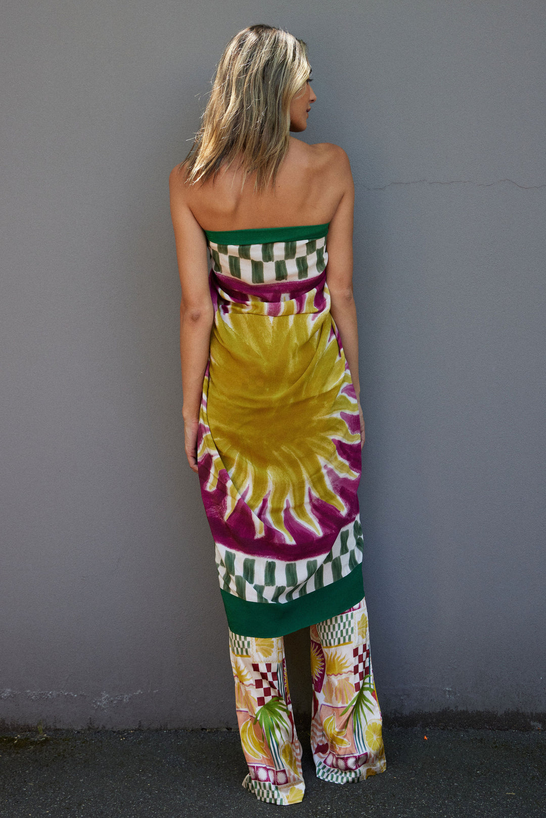 Woman wearing a colorful sarong with a hand painted sun pattern against a gray wall.