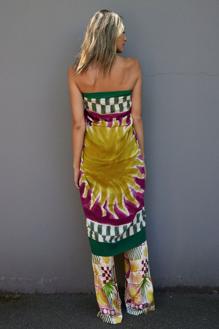 Woman wearing a colorful sarong with a hand painted sun pattern against a gray wall.