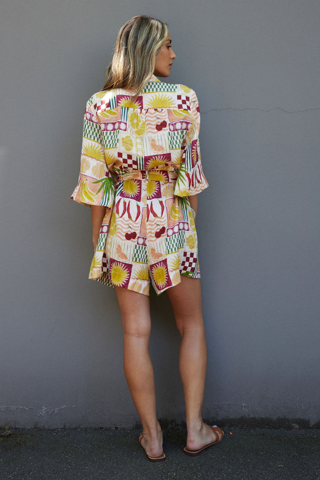 Woman wearing a colorful patterned outfit against a gray wall