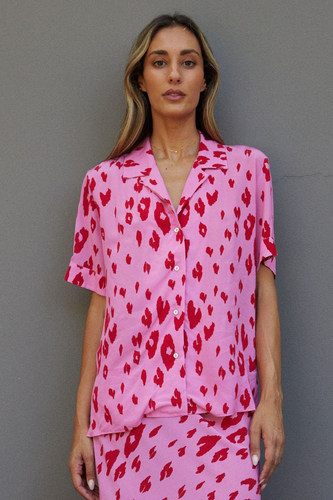 Woman wearing a pink outfit with red leopard print against a gray wall.