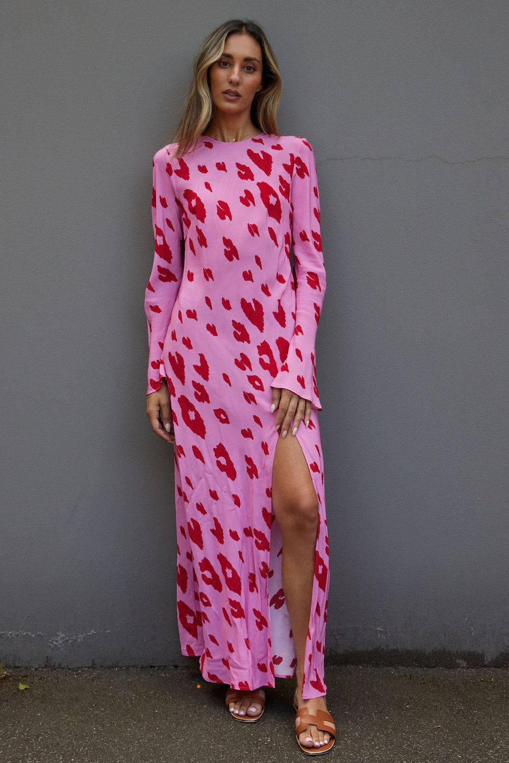 Woman wearing a pink dress with red leopard print against a gray wall.
