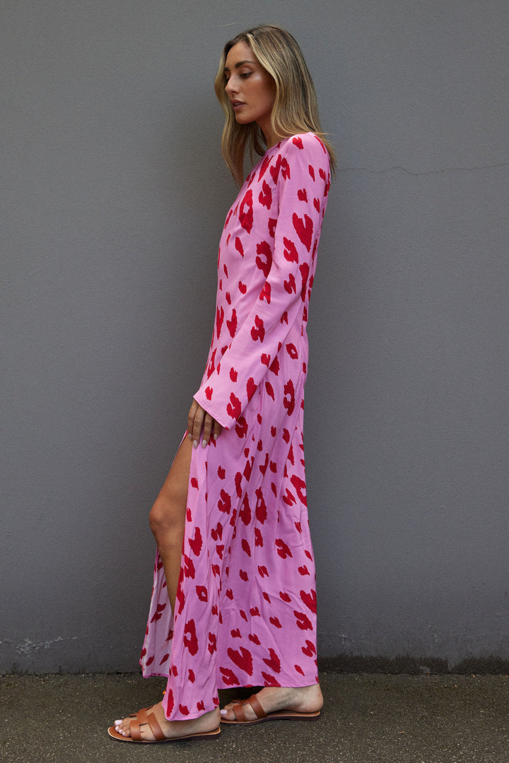 Woman wearing a pink dress with red patterns against a gray wall