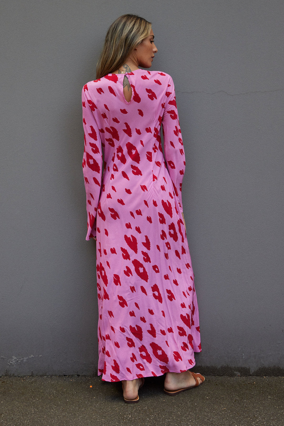 Woman wearing a pink dress with red patterns against a gray wall