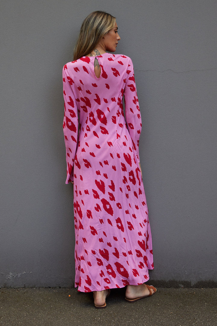 Woman wearing a pink dress with red patterns against a gray wall