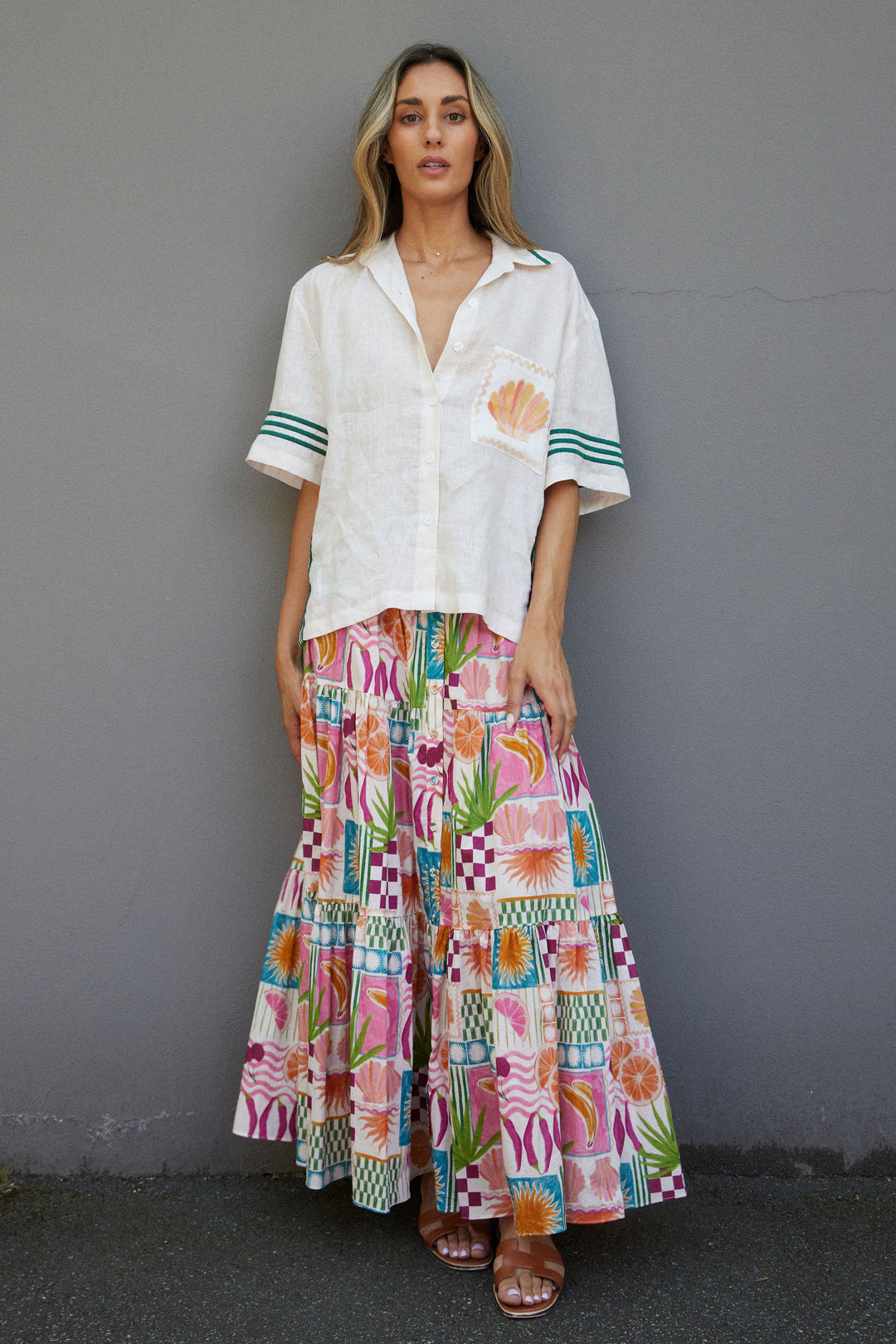 Woman wearing a white shirt and colorful patterned skirt against a gray wall.