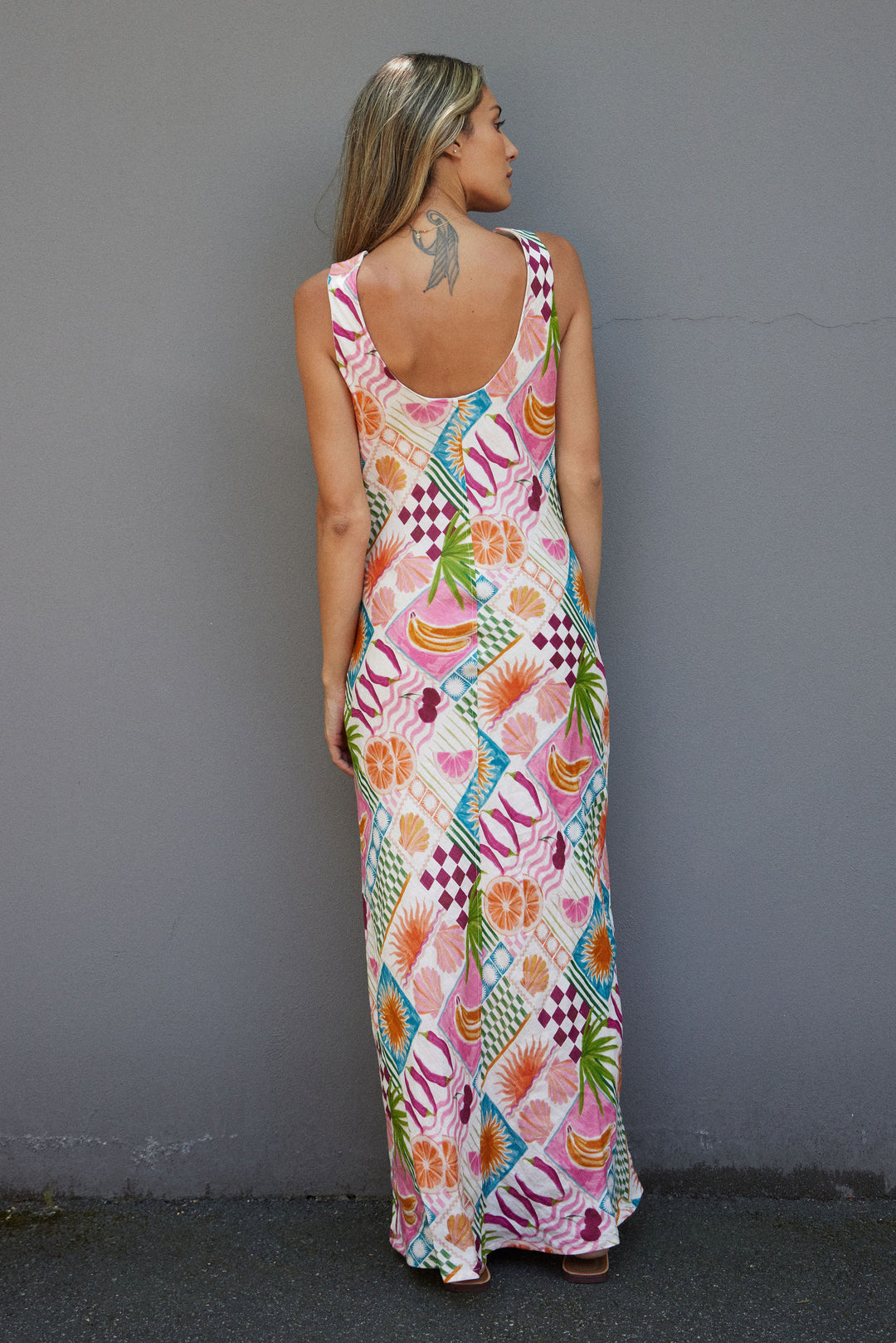 Woman wearing a colorful patterned dress against a gray wall.
